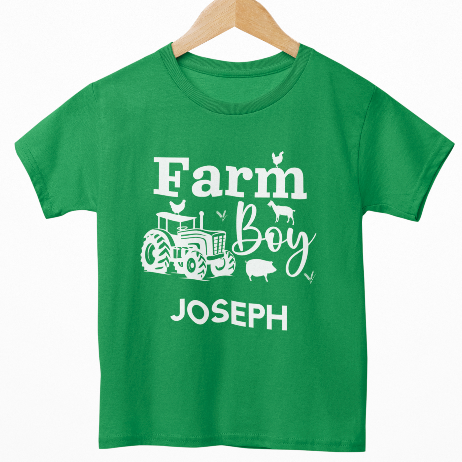 Kids green “Farm Boy” T-shirt with white tractor and farm animals design, personalised with the name in white text underneath. Styled on a wooden hanger.