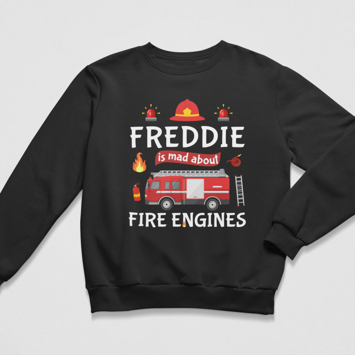 A kids black crewneck sweatshirt featuring a graphic design of a red fire truck, firefighter helmet, and flames, with the text 'FREDDIE is mad about FIRE ENGINES' printed on the front, displayed on a light grey background.