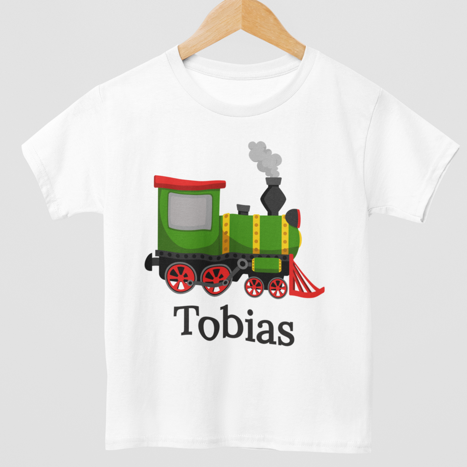 Close up of kids personalised steam train t-shirt with green and red locomotive graphic - white tee styled on a wooden hanger.