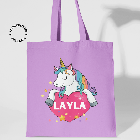 Lavender cotton tote bag with a white unicorn holding a pink heart featuring the name “Matilda.” Surrounded by stars, ideal for carrying books, toys, or lunch.