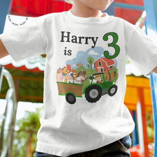 A boy at the park wearing a white personalised birthday t-shirt with a printed design of farm animals, green tractor, number 3 and custom name