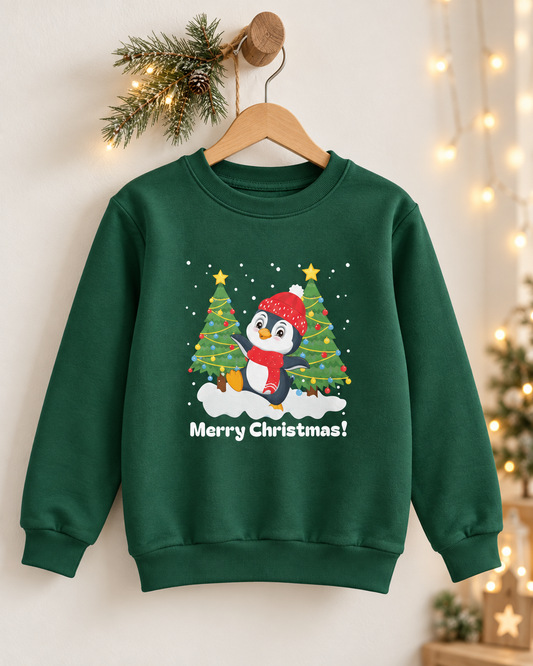 Dark green children’s penguin Christmas sweatshirt on a wooden hanger, with a pine sprig and warm fairy lights against a light wall.