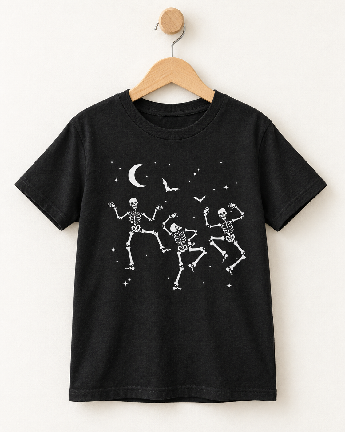 Kids’ black dancing skeletons Halloween T-shirt displayed on a wooden hanger and wall hook.