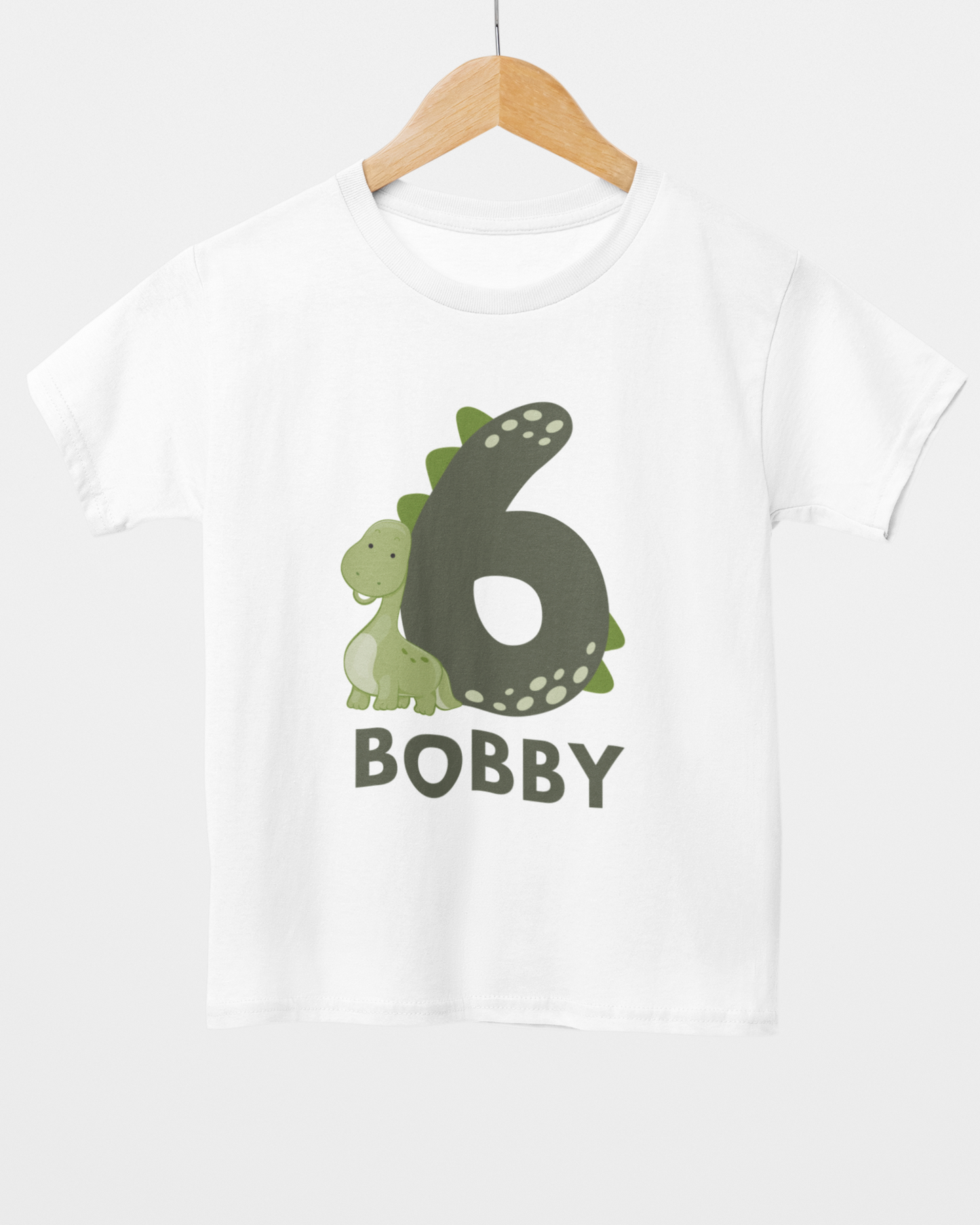 Personalised 6th birthday dinosaur t-shirt with name Bobby, minimal sage green number six birthday shirt on wooden hanger