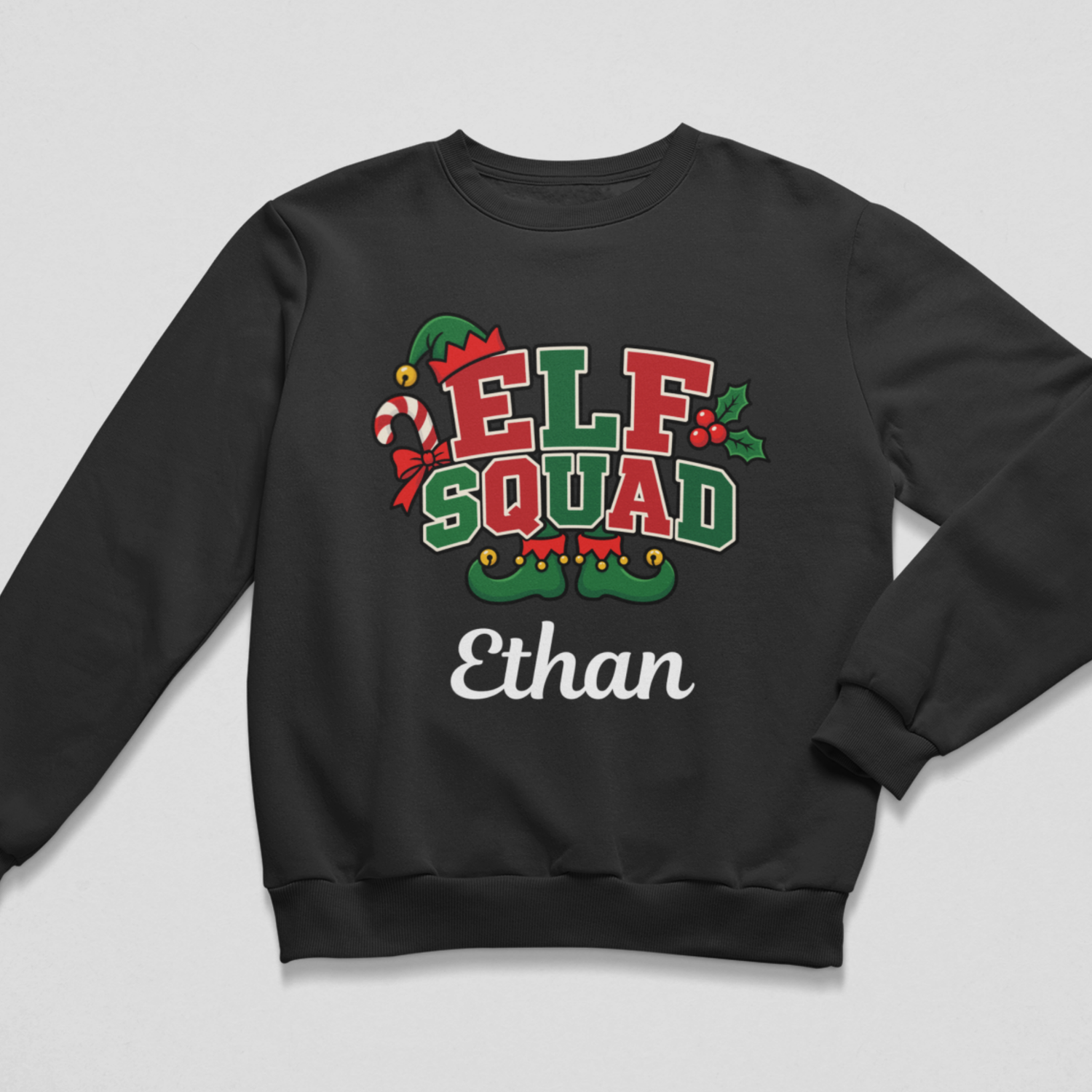 Flat lay of a black kids' Christmas crewneck sweatshirt featuring a festive "ELF SQUAD" graphic decorated with a candy cane, holly leaves, and elf shoes, with the personalised name "Ethan" printed below in white script.