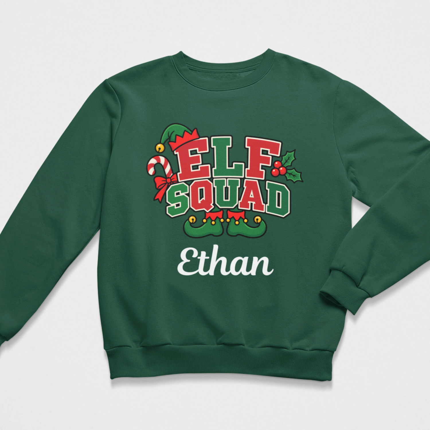 Flat lay of a dark green kids' Christmas crewneck sweatshirt featuring an "ELF SQUAD" holiday graphic with a candy cane and elf shoes, alongside the personalized name "Ethan