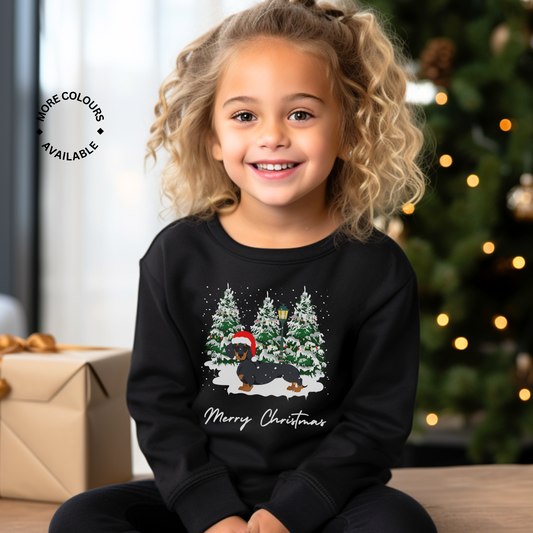 A child wearing a black sweatshirt with a Christmas-themed graphic including a dachshund wearing a Santa hat, surrounded by snow and trees, with the text 'Merry Christmas'.