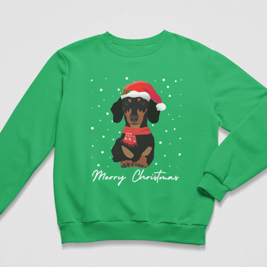 A kids green crewneck sweatshirt featuring a graphic of a dachshund wearing a red Santa hat and scarf, surrounded by white snowflakes, with 'Merry Christmas' written in white script below.