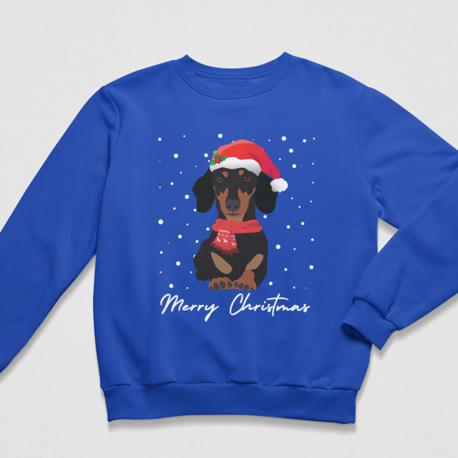 A kids royal blue crewneck sweatshirt featuring a graphic of a dachshund wearing a Santa hat and scarf, surrounded by white snowflakes, with 'Merry Christmas' written in white script below.