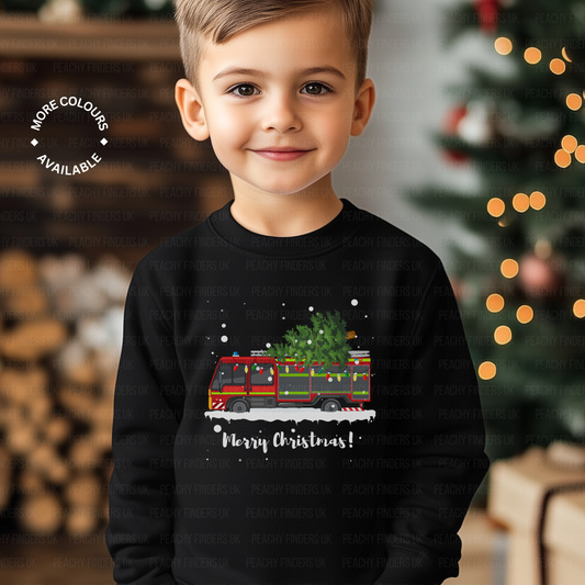 Smiling boy wearing a black kids Christmas sweatshirt featuring a festive fire engine carrying a decorated Christmas tree and the text "Merry Christmas!"