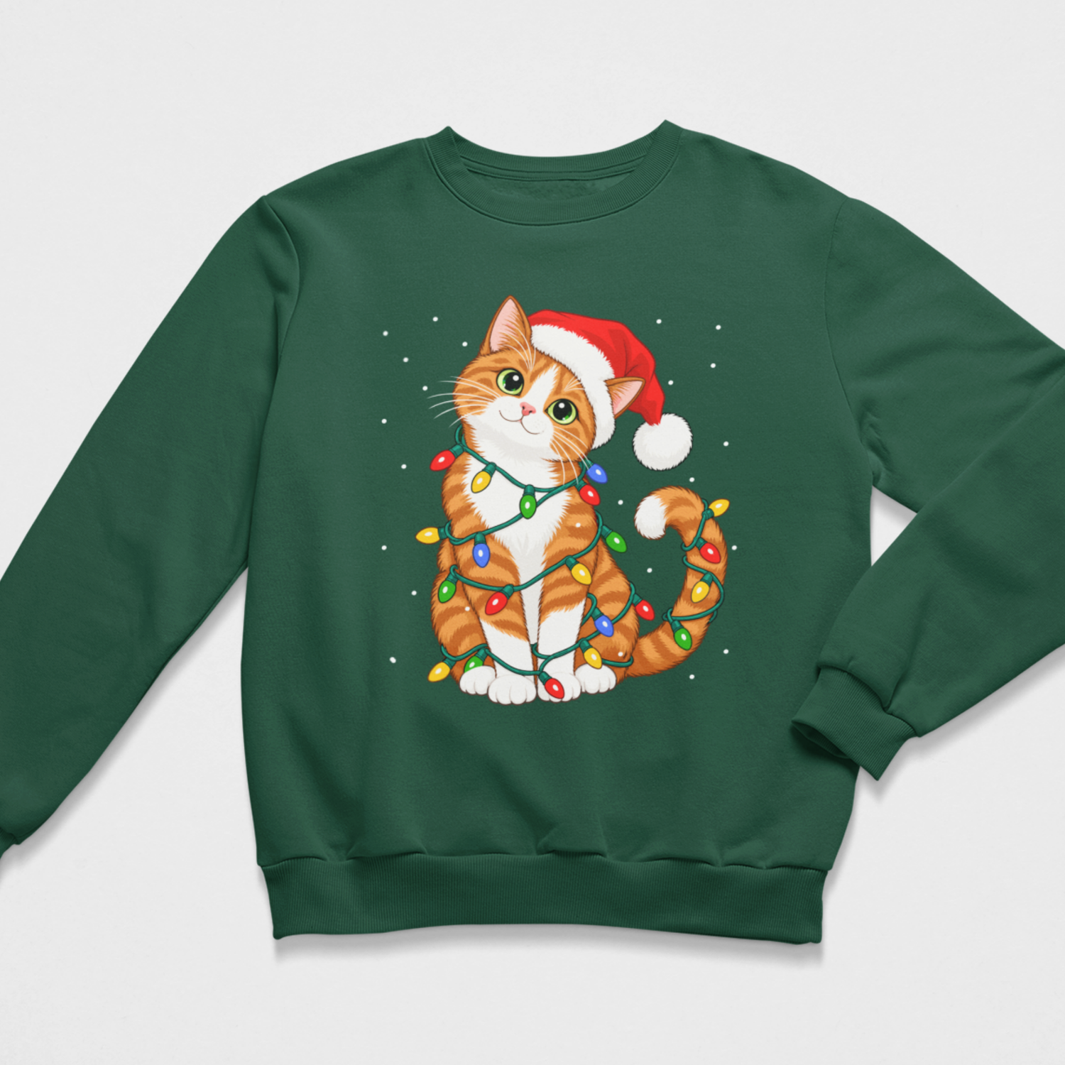 Flat lay of a dark green kids' Christmas crewneck sweatshirt featuring an orange and white tabby cat wearing a red Santa hat and wrapped in colourful festive fairy lights, set against a snowy background.