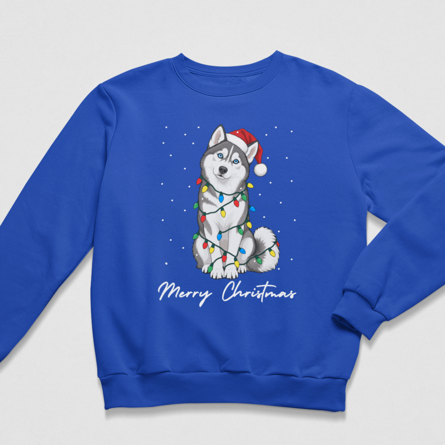 Children's royal blue crewneck sweatshirt featuring a graphic of a grey and white husky dog wearing a red Santa hat and wrapped in multicoloured Christmas lights, with 'Merry Christmas' written below in white script.