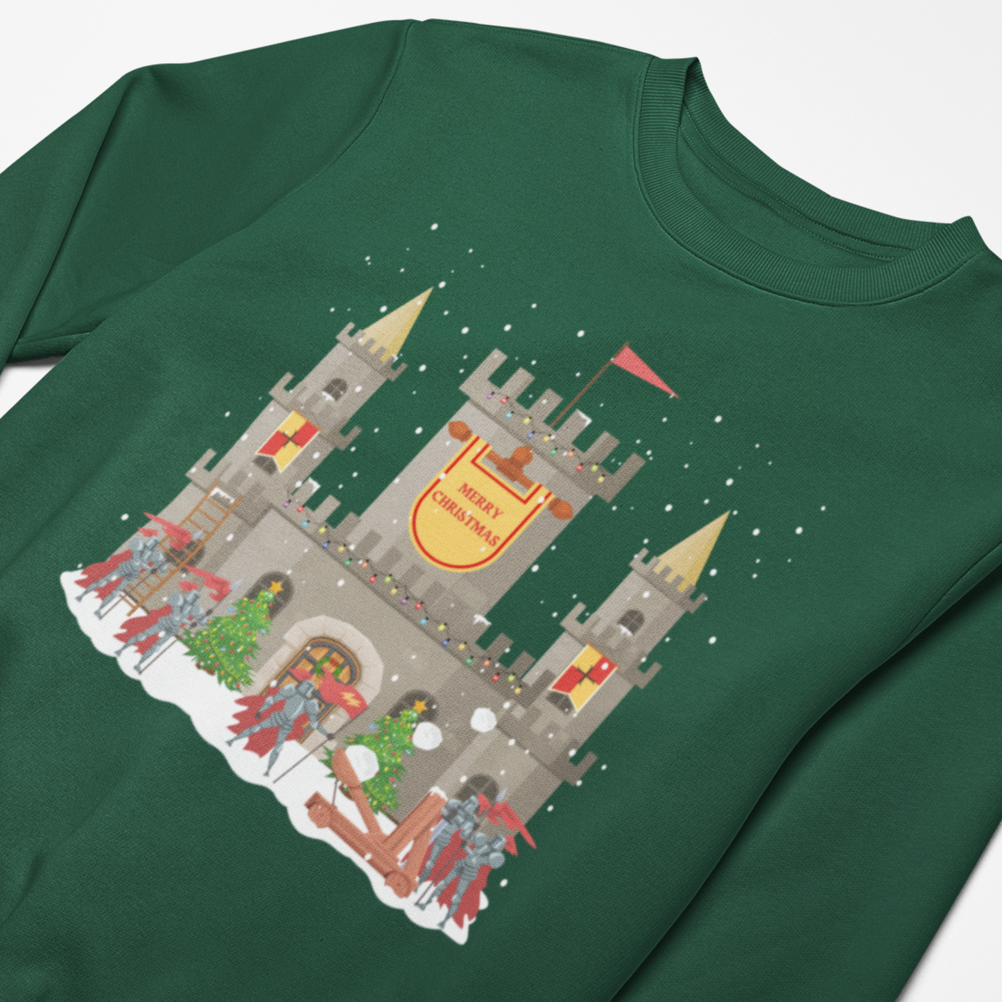 Close up dark green kids Christmas sweatshirt showing a snowy stone castle with “Merry Christmas” banner, golden turrets, red-armoured knights, catapult and festive trees on the front.