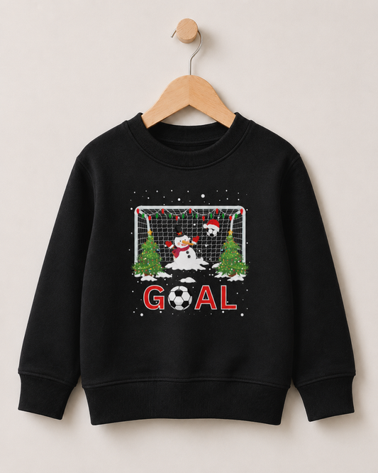 A kids black crewneck sweatshirt hanging on a wooden hanger against a light beige wall. The sweatshirt features a festive Christmas-themed soccer graphic with a snowman, a soccer ball, Christmas trees, a goal net, and the word 'GOAL' in red.