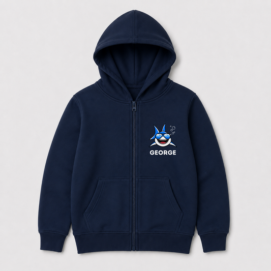 A navy blue zip-up hoodie for kids, featuring a front pocket, a blue cartoon shark graphic with sunglasses on the left chest, and the name 'GEORGE' printed below it in white. The hoodie is displayed on a clean, light grey background.