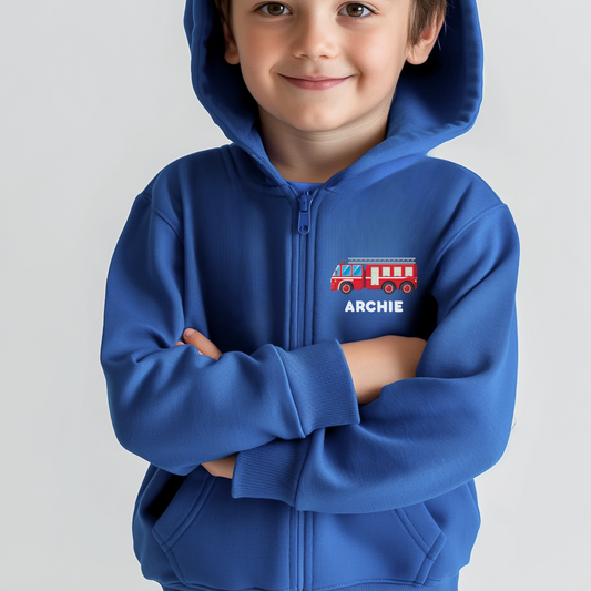 A little boy smiling and wearing a royal blue full zip hoodie with small printed motif of a red fire truck with the name Archie underneath
