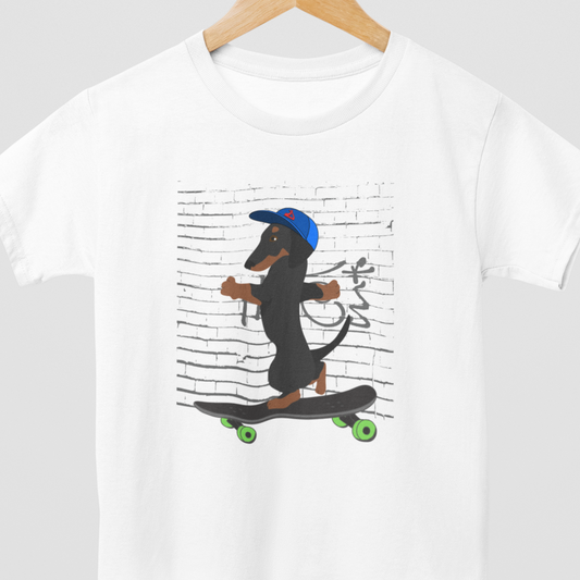 Kids white t-shirt  on a wooden hanger, featuring a cool printed graphic of a Dachshund Dog wearing a baseball cap riding a skateboard with green wheels