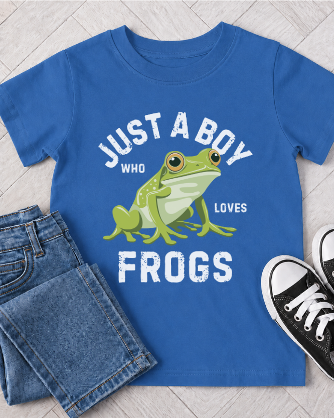 A royal blue kids t-shirt with a graphic of a green frog and the text 'JUST A BOY WHO LOVES FROGS', styled in a flat lay with blue jeans and black sneakers on a light wood floor.
