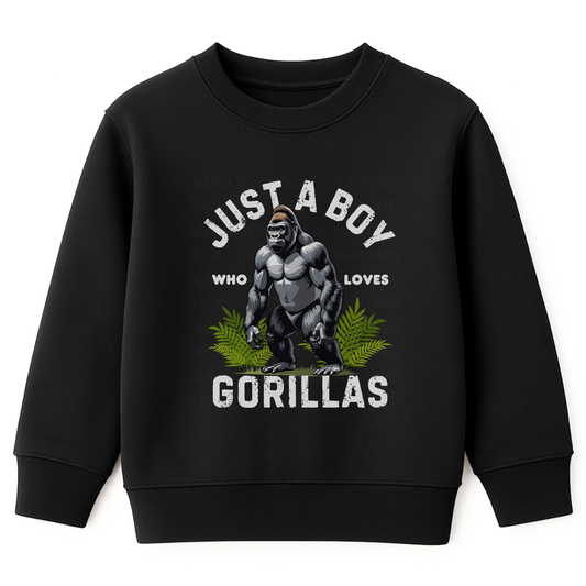 Kids black sweatshirt with “Just a Boy Who Loves Gorillas” text and gorilla graphic over green leaves, flat lay on white background.