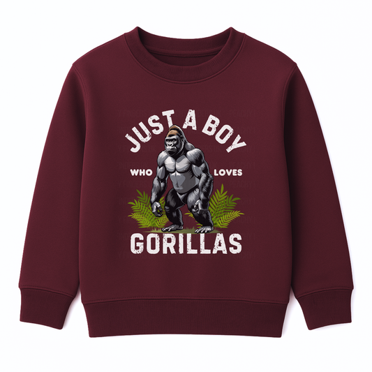 Kids burgundy sweatshirt with “Just a Boy Who Loves Gorillas” text and gorilla graphic over green leaves, flat lay on white background.