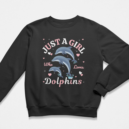 A kids black crewneck sweatshirt featuring a graphic print of three dolphins with the text 'JUST A GIRL Who Loves Dolphins' in pink and white lettering, surrounded by small pink hearts, on a light grey background.