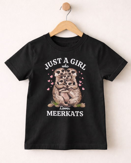 Kids “Just a Girl Who Loves Meerkats” graphic black t-shirt hanging on a wooden hanger against a cream wall background