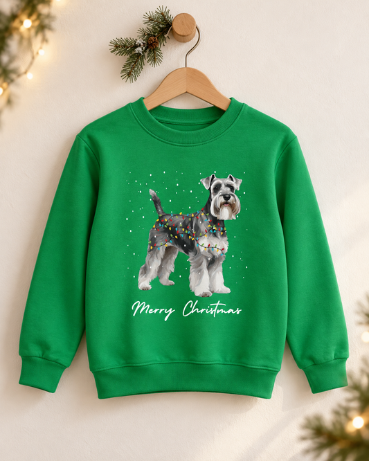 Kelly green kids Christmas Schnauzer sweatshirt hanging on a wooden wall peg against a neutral backdrop with festive pine sprig decor and fairy lights