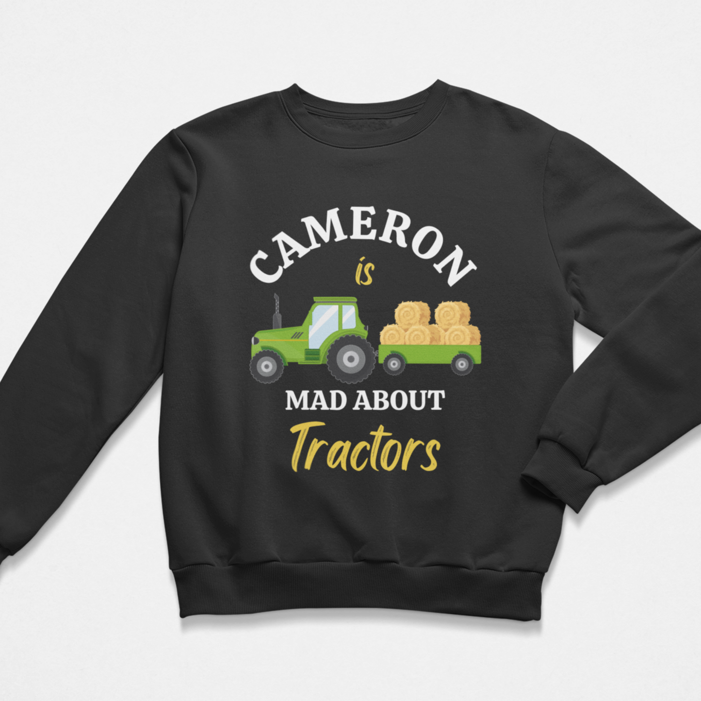 A kids black crewneck sweatshirt featuring a graphic print of a green tractor carrying hay bales, with the text 'CAMERON is MAD ABOUT Tractors' in white and yellow lettering.