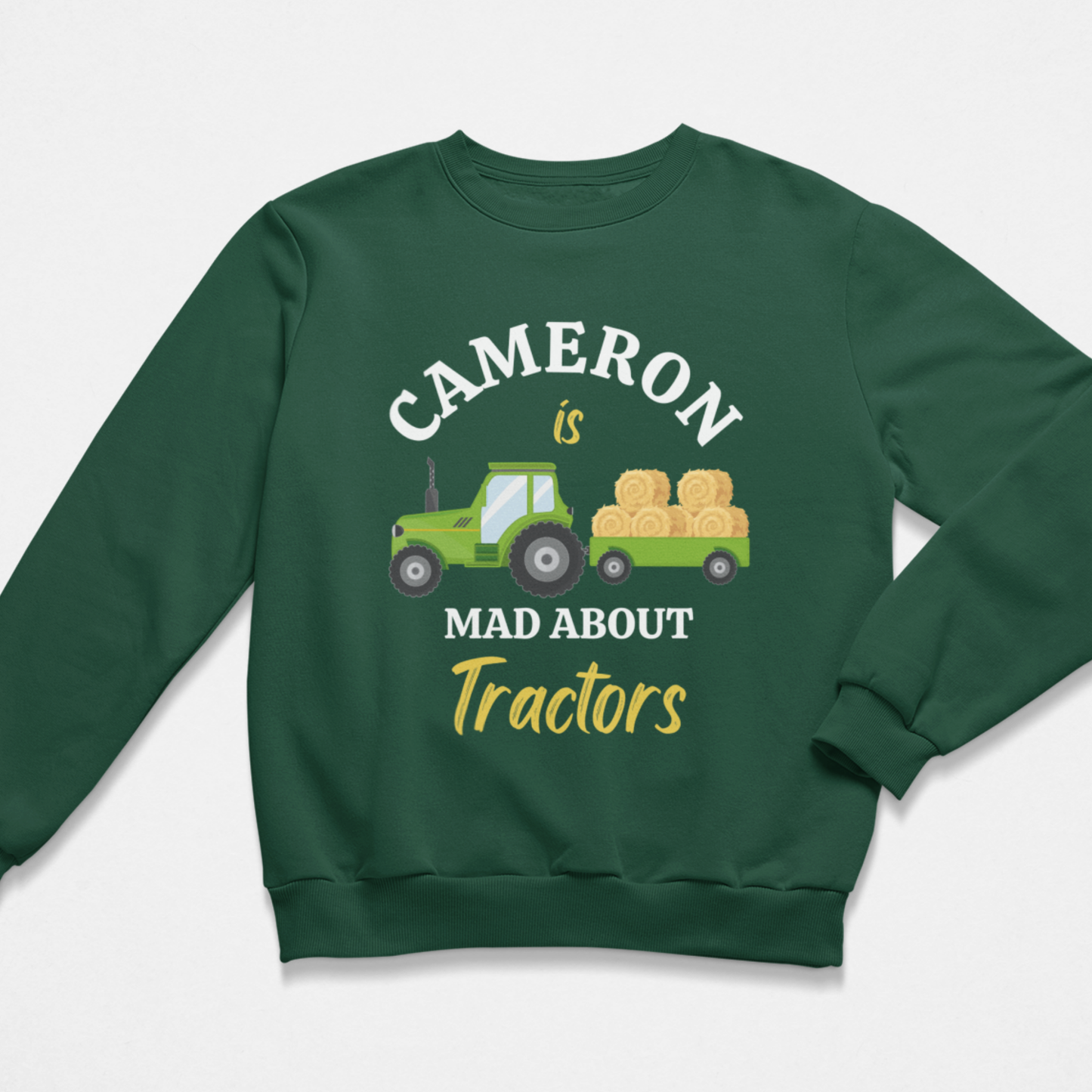A boys dark green crewneck sweatshirt featuring a graphic print of a green tractor carrying hay bales, with the text 'CAMERON is MAD ABOUT Tractors' in white and yellow lettering.