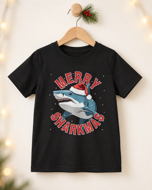 Black kids’ Christmas T-shirt featuring a shark in a Santa hat with red Merry Sharkmas lettering, displayed on a wooden hanger.