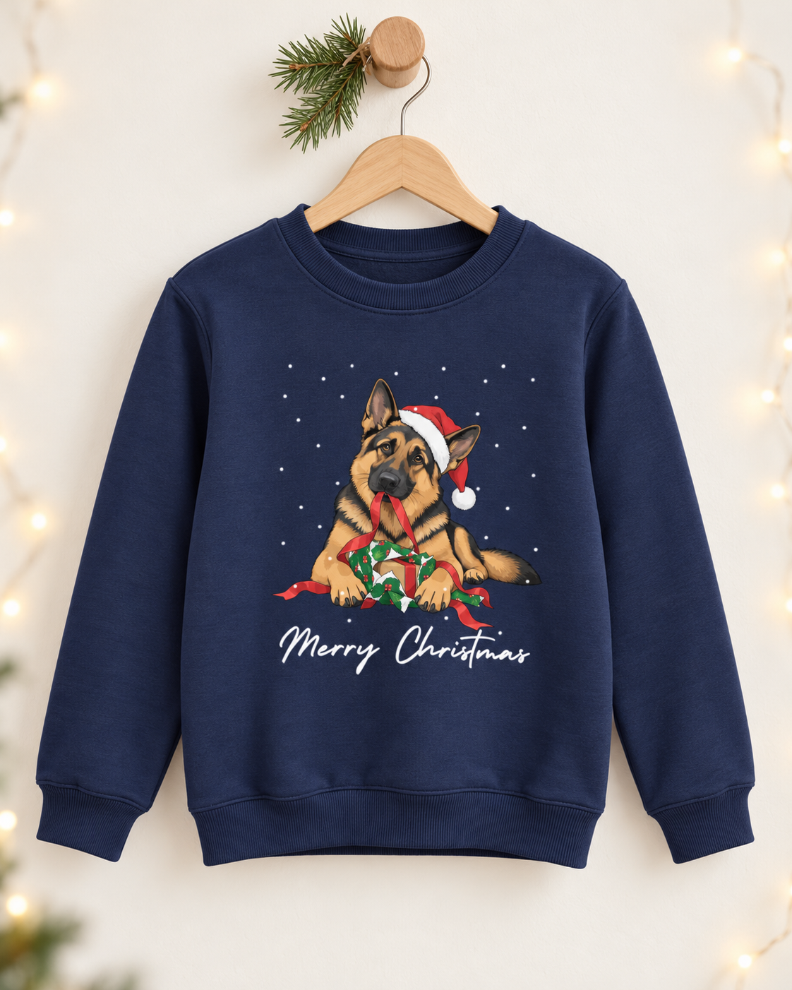 A navy blue crewneck sweatshirt hanging on a wooden hanger against a warm, softly lit background. The sweatshirt features a graphic of a German Shepherd dog wearing a Santa hat and holding a wrapped Christmas gift, with 'Merry Christmas' written in white script below.