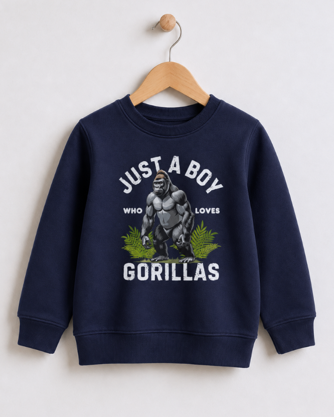 A kids navy blue crewneck sweatshirt hanging on a wooden hanger against a light grey wall. The sweatshirt features a graphic print of a gorilla with green leaves and white text that reads 'JUST A BOY WHO LOVES GORILLAS'.