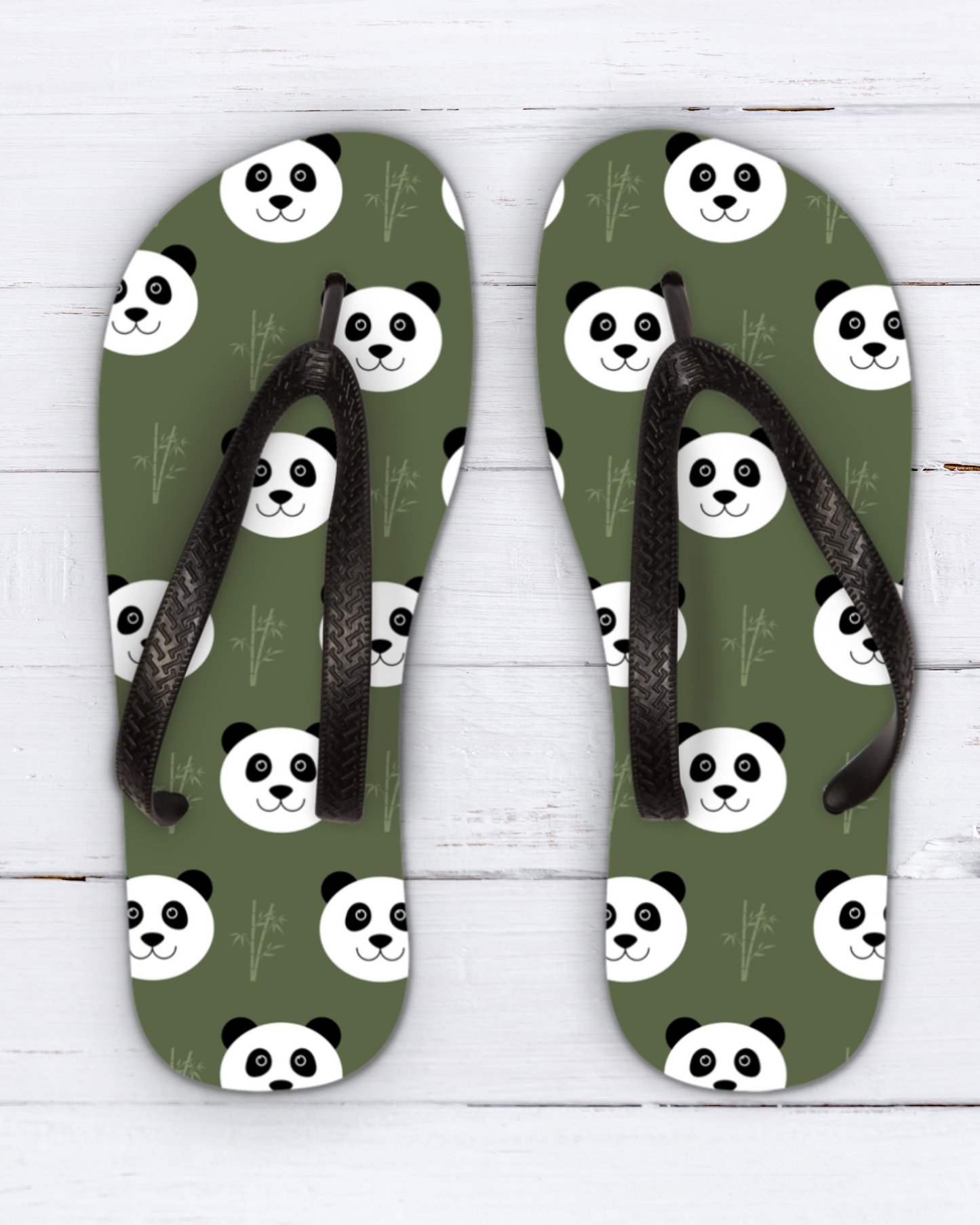 A pair of kids olive green flip-flops with a repeating panda face pattern and black straps, displayed flat on a white wood background.