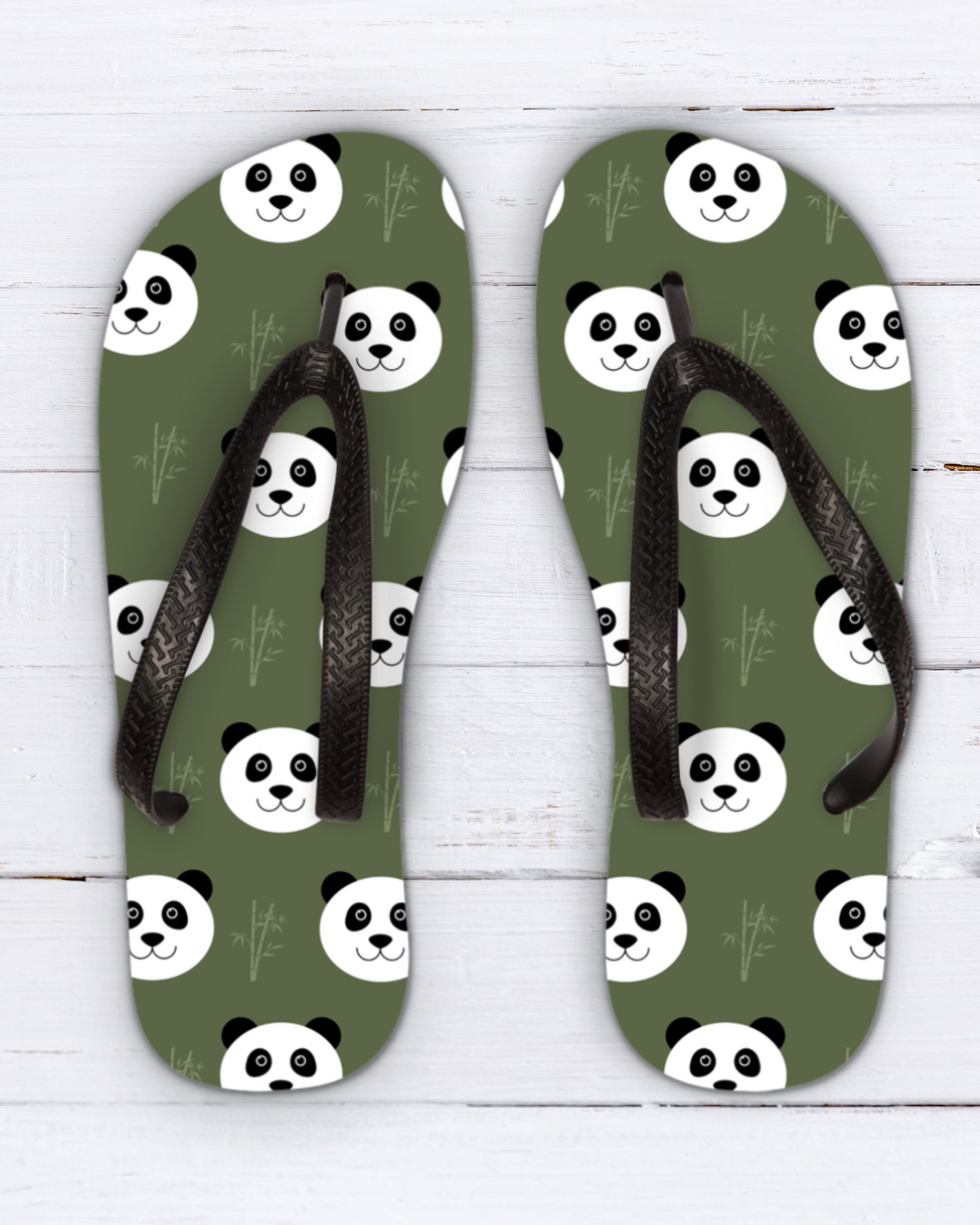 A pair of kids olive green flip-flops with a repeating panda face pattern and black straps, displayed flat on a white wood background.