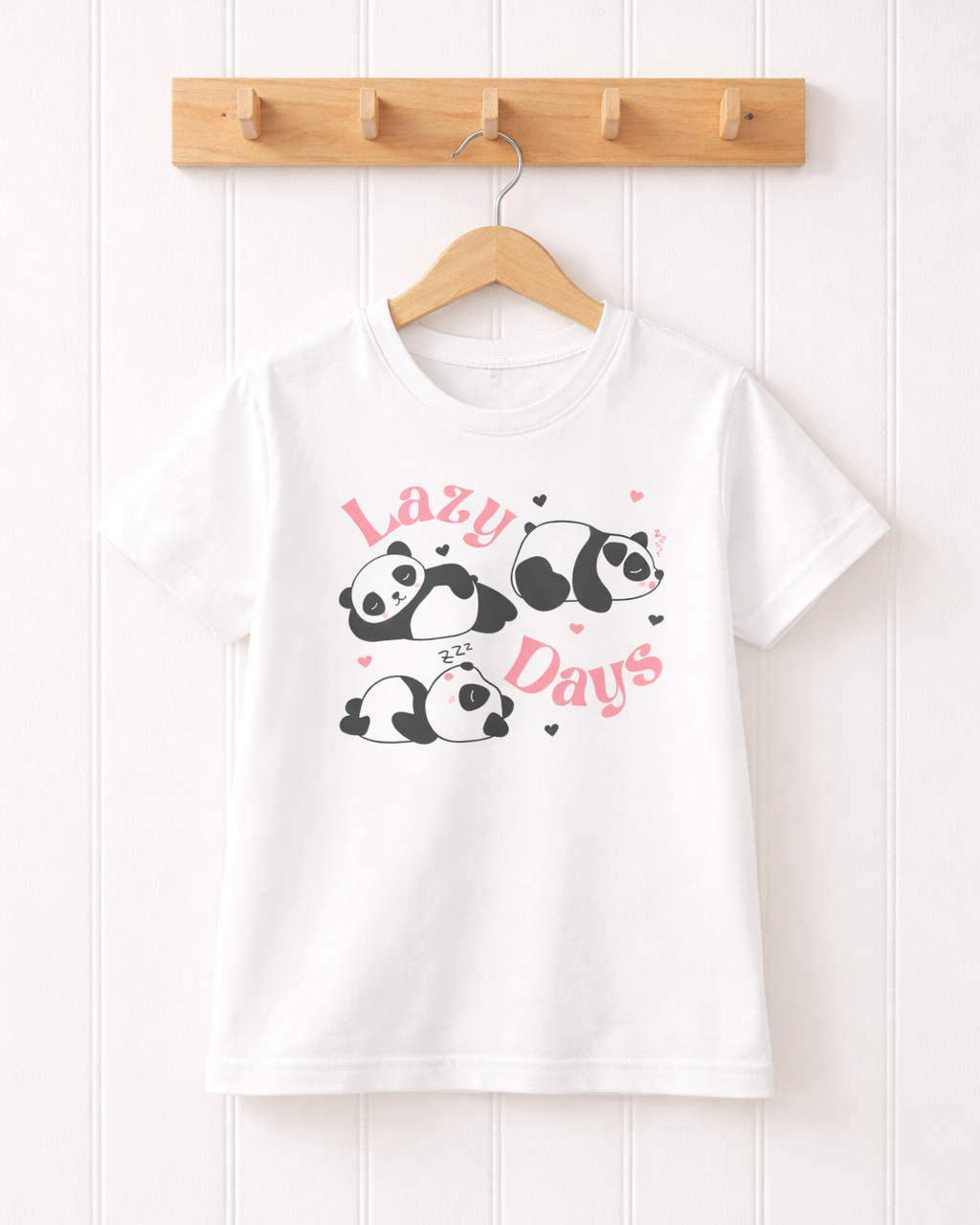 White “Lazy Days” panda kids t-shirt hanging on a wooden hanger on a wooden hook against a white panelled wall background.