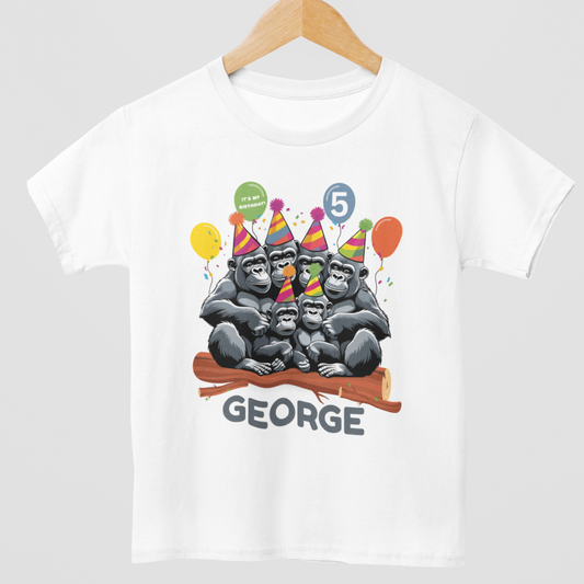 A kids personalised birthday t-shirt in white with a fun Gorilla family wearing party hats, sitting on a log with balloons and falling confetti - styled on a wooden hanger.