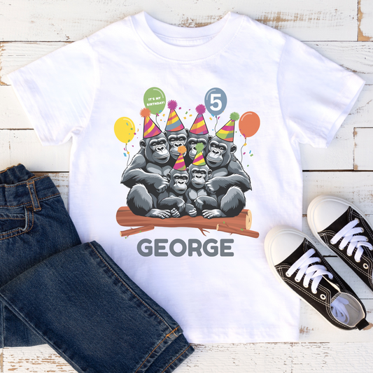 White t-shirt with gorilla birthday design, jeans, and sneakers on a wooden surface