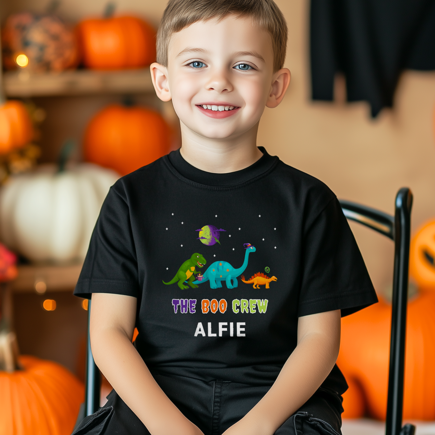 Child wearing a personalised black Halloween T-shirt with colourful dinosaur characters and the phrase “The Boo Crew” above the name “Alfie”.