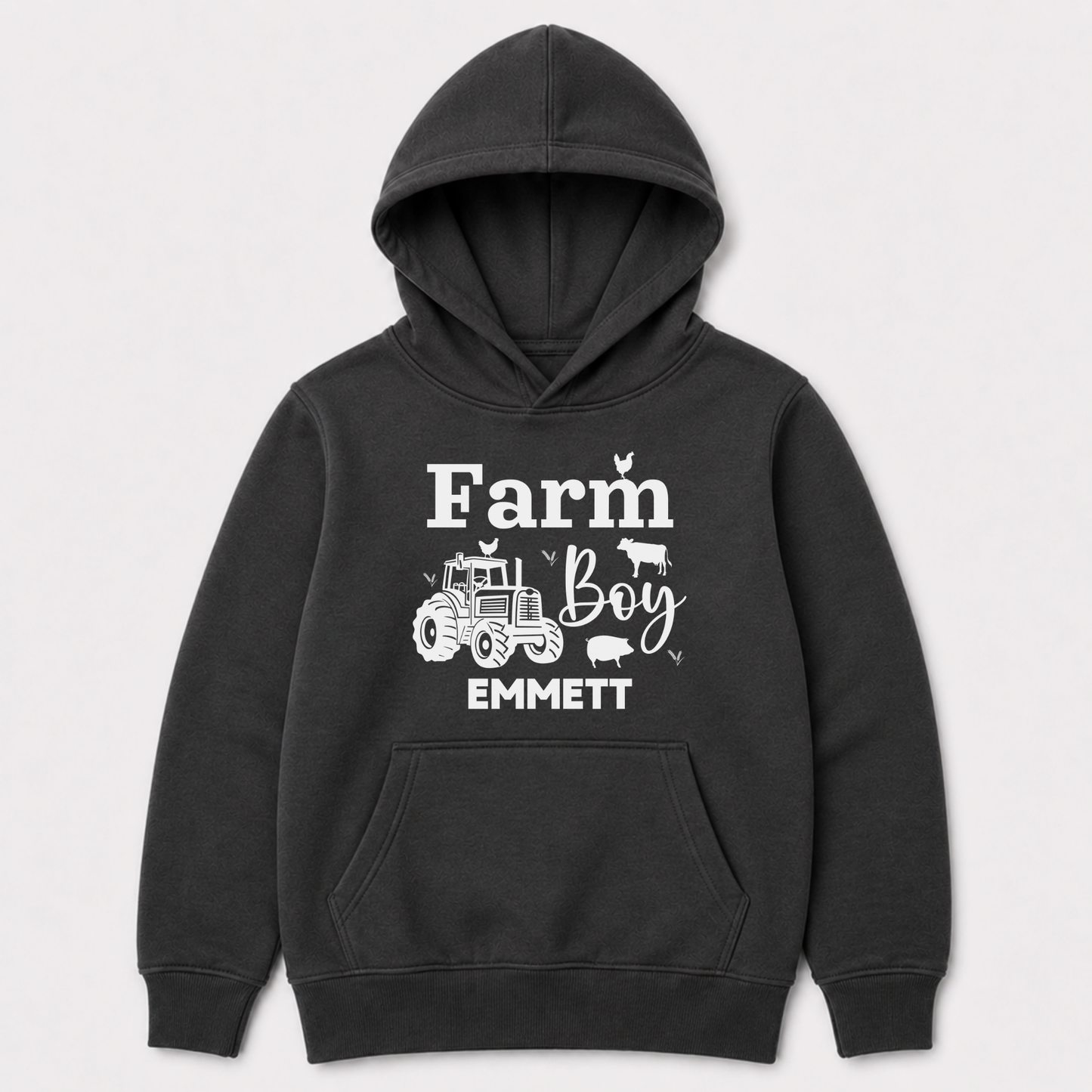 A dark grey pullover hoodie for kids with a white graphic print on the front that reads 'Farm Boy EMMETT' with illustrations of a tractor, cow, chicken, and pig, shown against a light grey background.