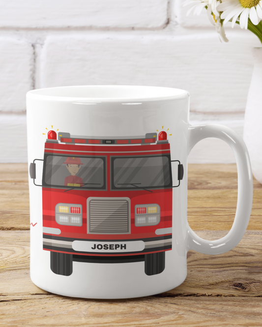 A white mug with a kids personalised fire engine design featuring a character in a fire engine, with the name 'Joseph' printed on the number plate.