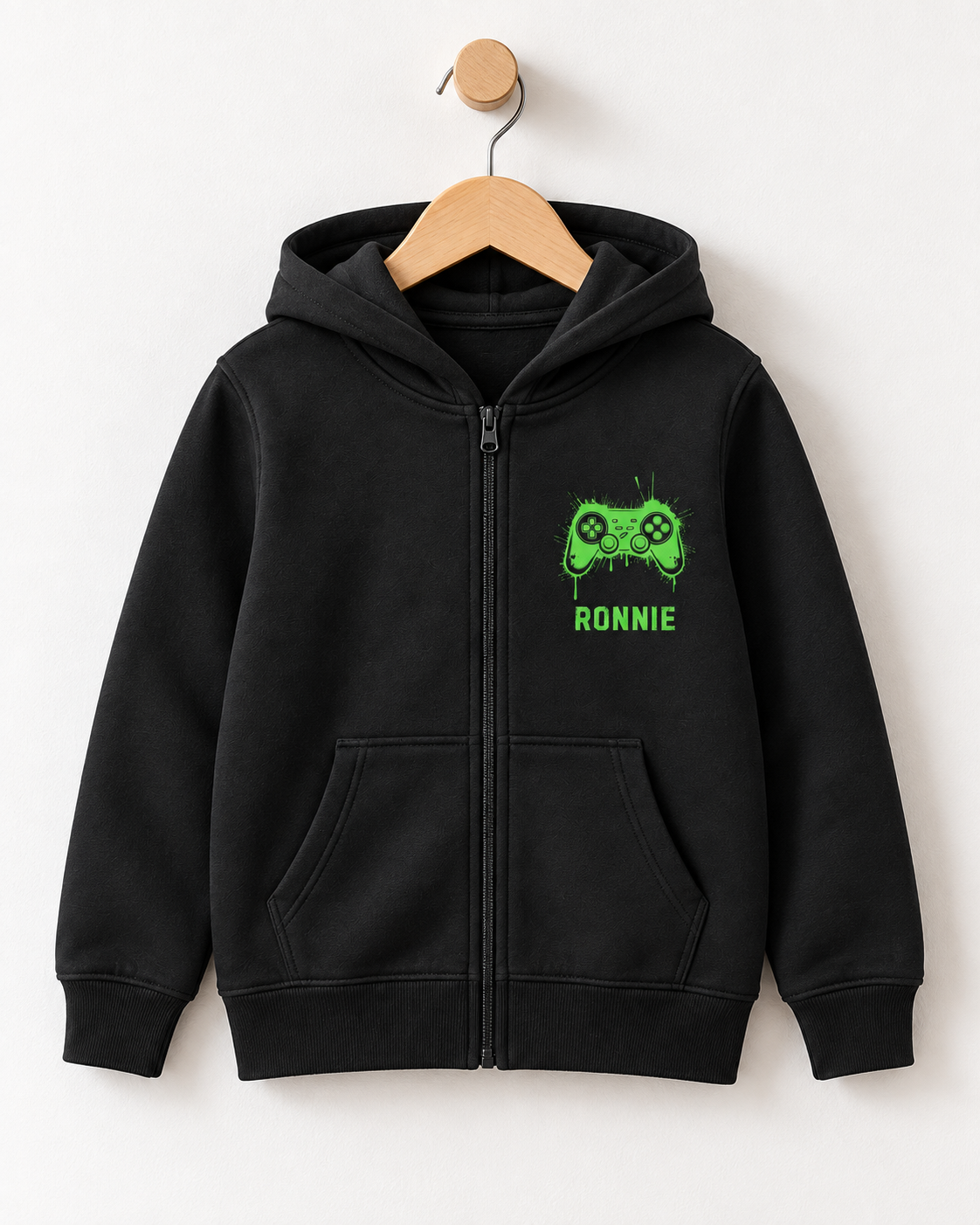 Black kids’ personalised zip hoodie on a wooden hanger, with a neon green graffiti-style gaming controller and the name Ronnie on the chest.