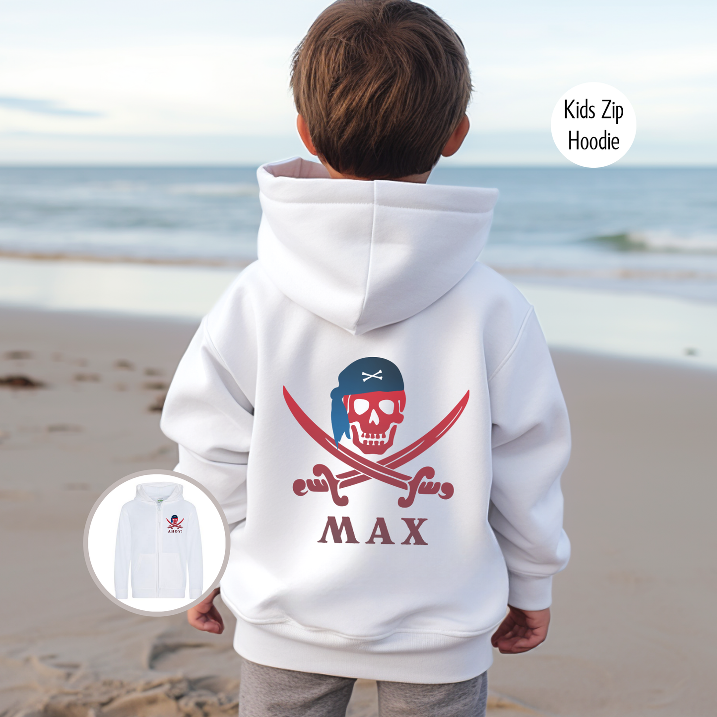 A child standing on a beach wearing a white zip hoodie with a personalised pirate skull graphic and the name 'MAX' printed on the back.