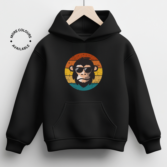 Black kids' hoodie with a graphic of a chimp wearing sunglasses against a multicolored circular background, positioned on a hanger.