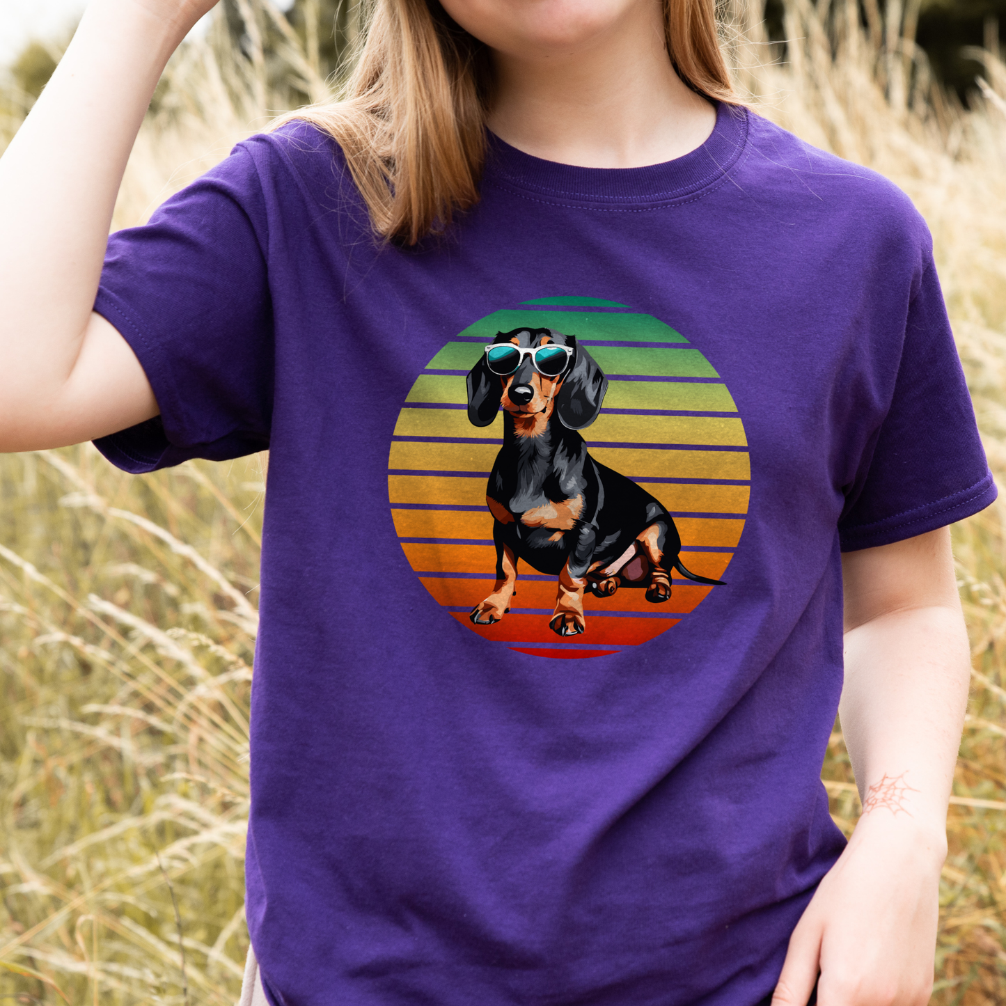 Young girl wearing a purple t-shirt with cool summer dachshund wearing sunglasses on a retro sunset background