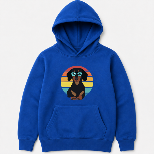A kids royal blue pullover hoodie featuring a graphic of a dachshund wearing round sunglasses, set against a retro sunset circle in shades of orange, yellow, and blue.