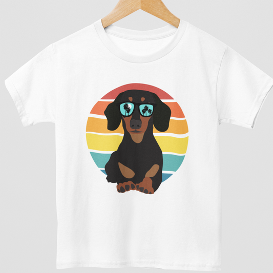 Kids short sleeved white t-shirt with a retro dachshund in sunglasses graphic styled on a wooden hanger.
