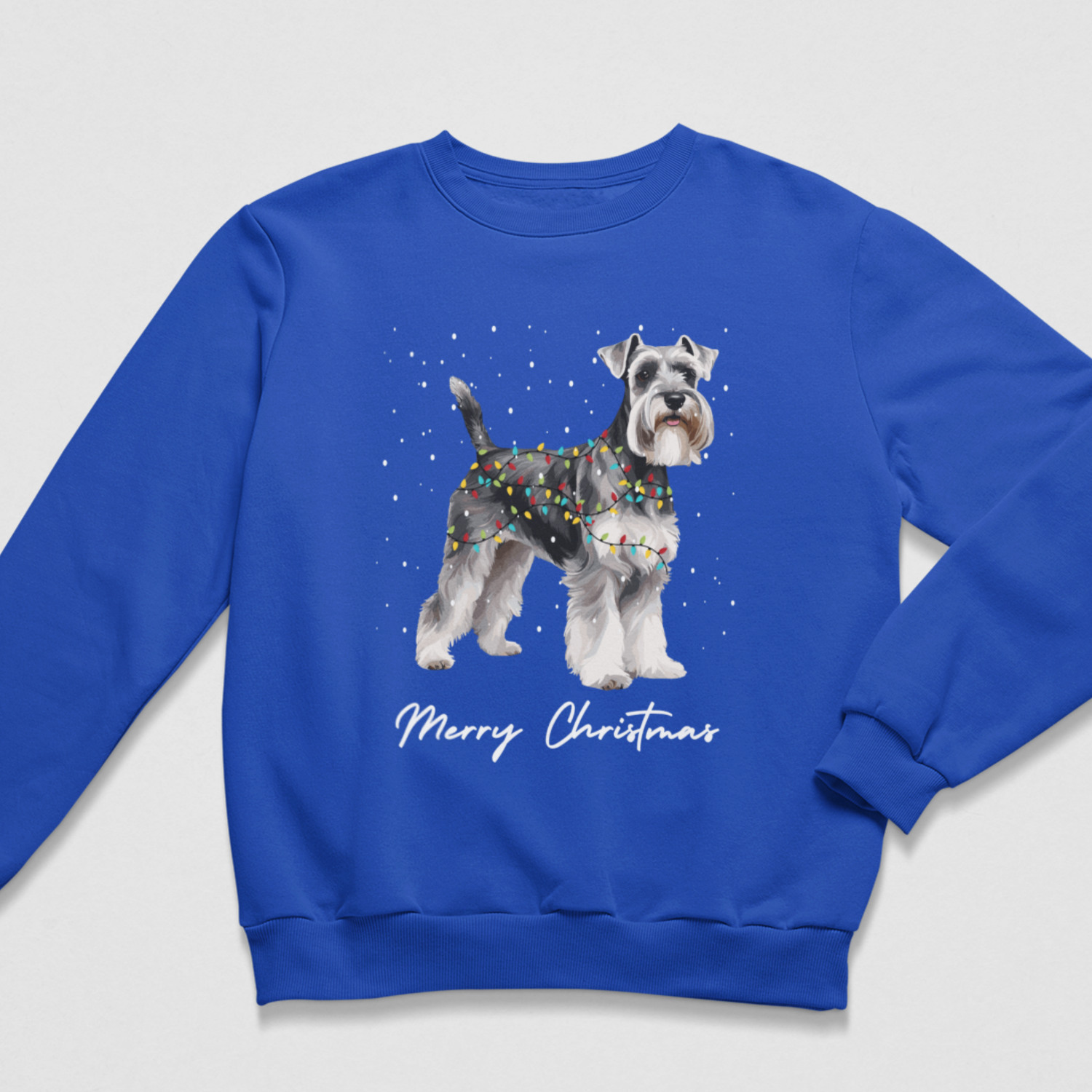 Royal blue children's Christmas jumper laid flat, featuring a pepper-and-salt Schnauzer wrapped in holiday lights under falling snow.