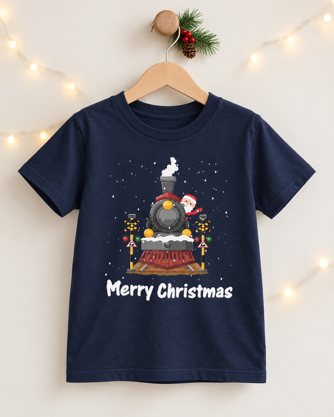 Navy kids Santa steam train Christmas T-shirt on a wooden hanger, featuring falling snow and Merry Christmas lettering.