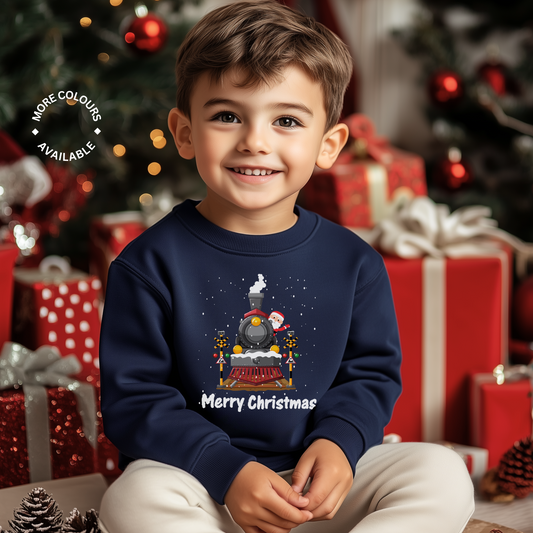 Little boy wearing a navy Christmas sweatshirt featuring a graphic of a festive black steam train decorated with snow and Santa Claus waving from the train. 'Merry Christmas' text is printed below the train, with white falling snow.