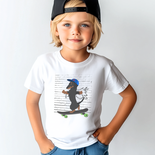 A young boy wearing a black backwards cap, modelling a white short sleeved t-shirt with printed design of a dachshund dog riding a skateboard